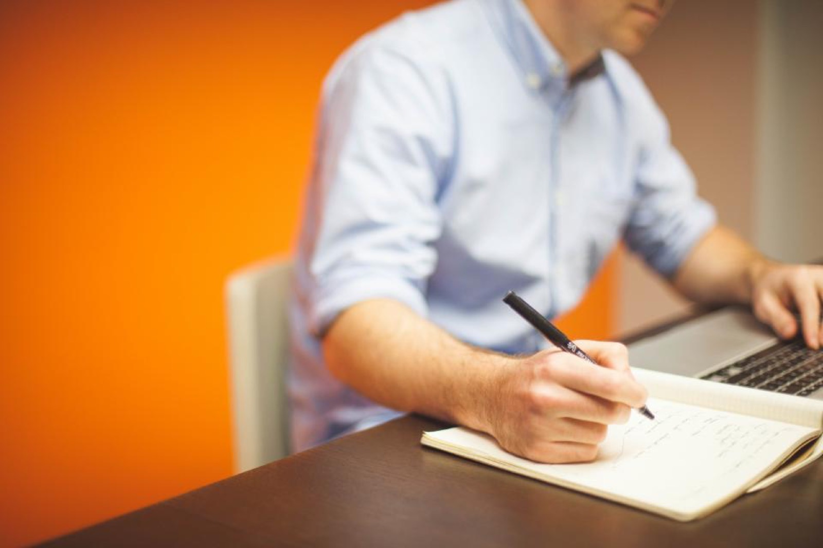 Personne prenant des notes dans un carnet à côté d'un ordinateur portable