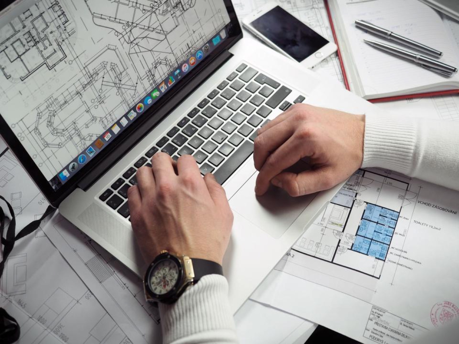 Mains sur un ordinateur portable entouré de plans techniques