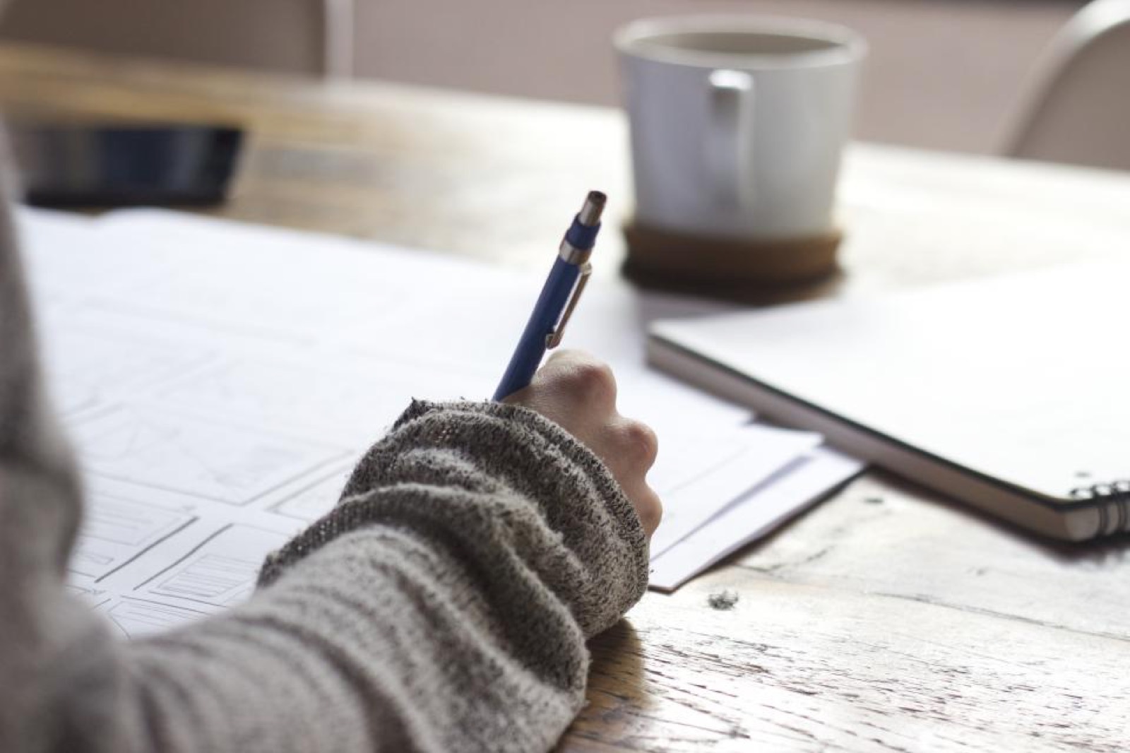 Main dessinant des maquettes de pages web sur papier, à côté d'un café