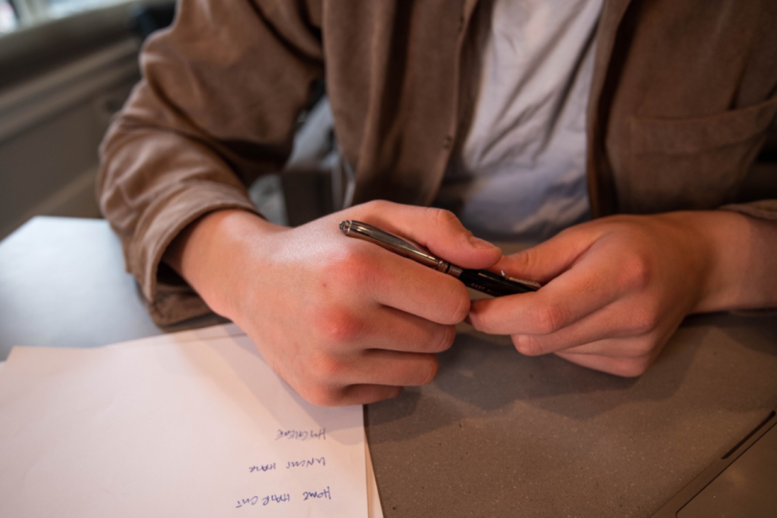 Mains tenant un stylo au-dessus de feuilles annotées posées sur un bureau