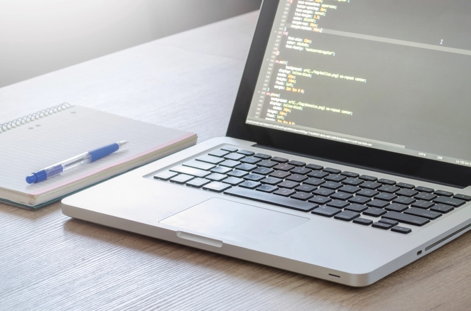 Ordinateur portable affichant du code CSS à côté d'un carnet et d'un stylo