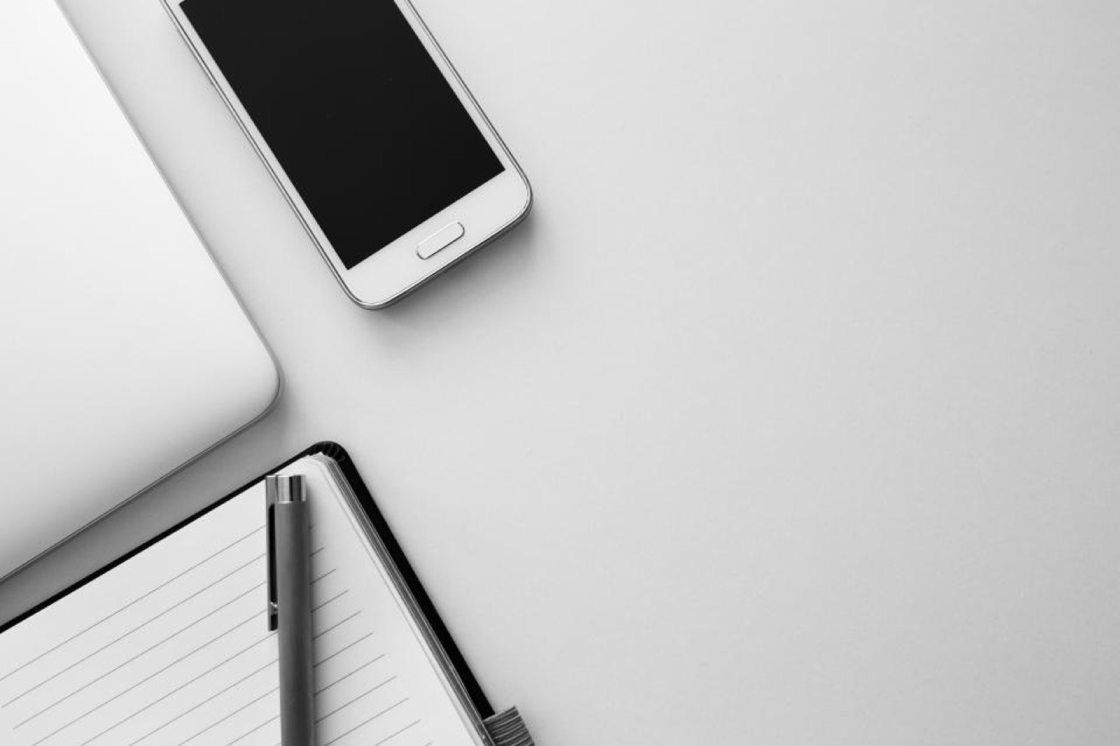 Smartphone, ordinateur portable fermé et carnet posés sur un bureau blanc